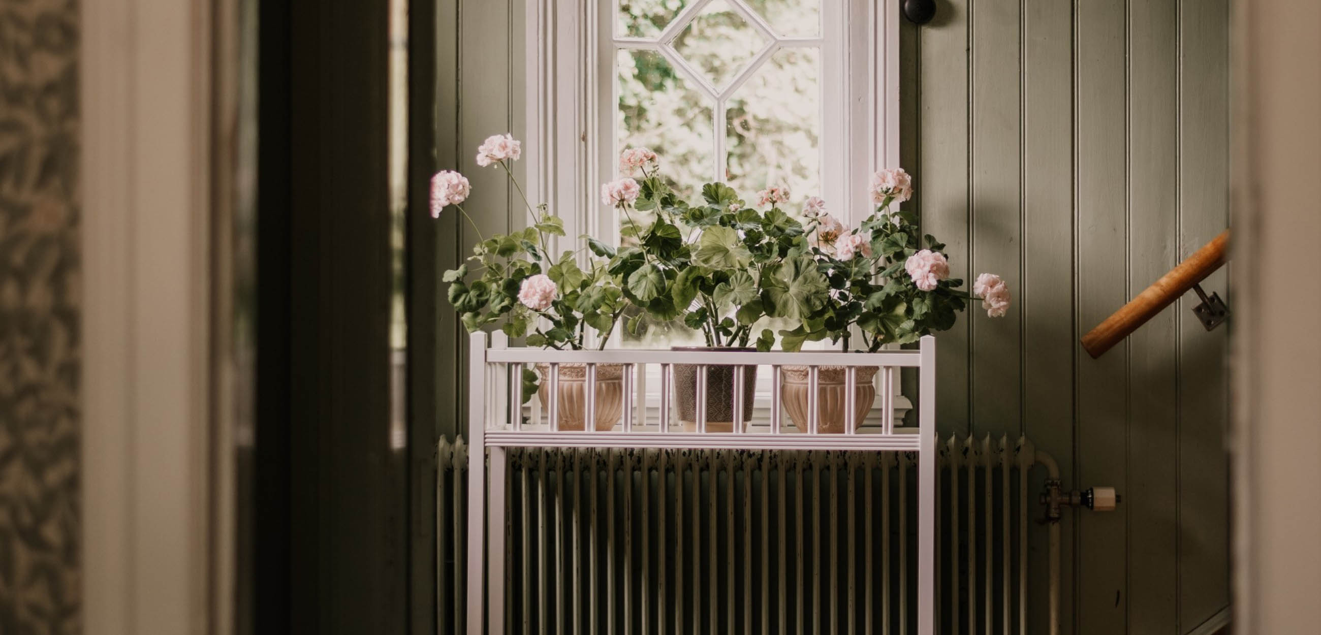 Vitt blombord med rosa blommor som är placerat under ett fönster